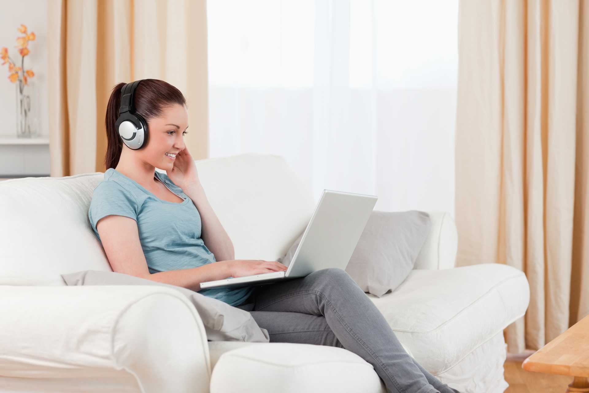 Kobieta siedząca na kanapie i pracująca na laptopie ze słuchawkami