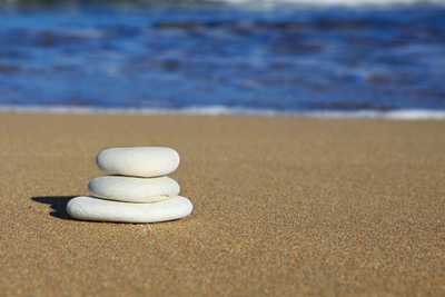 Trzy białe, płaskie kamienie ułożone na sobie na plaży, w tle morze