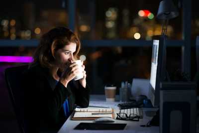 osoba pracująca po godzinach przed komputerem pijąca kawę